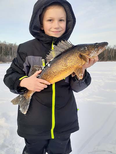 A young boy dressed in a winter coat holds a walleye caught while ice fishing