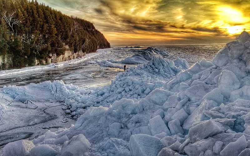 Ice shoves take on the shape of an iceberg near a lakeshore against an amber sky