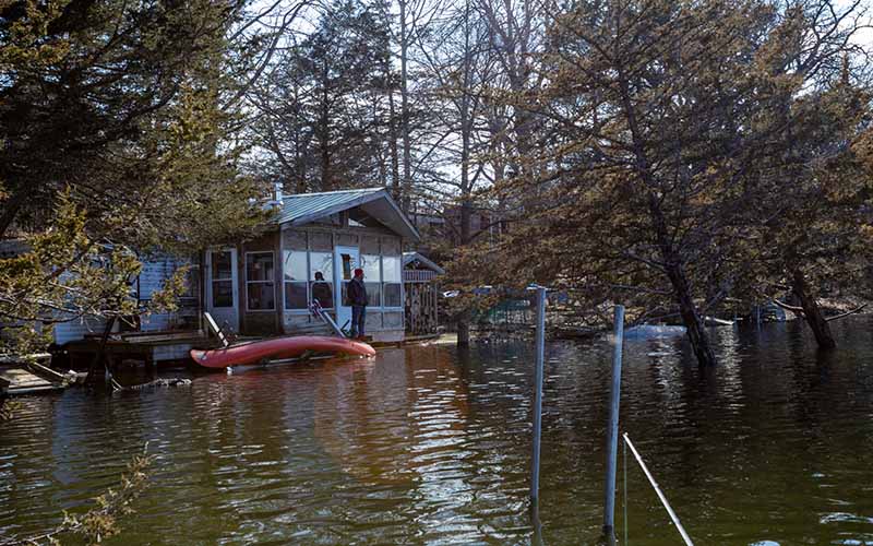 A homeowner stands on his front porch as his house is surrounded by flooding waters