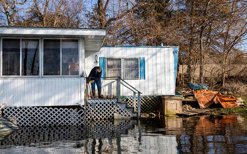 A woman stands on the porch of her mobile home as flood waters rise above its foundation