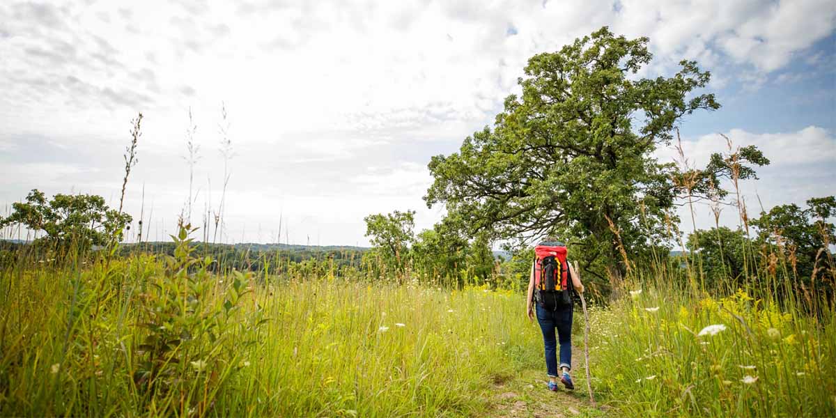 A backpacker hikes on a trail through a prairie on a partly cloudy day