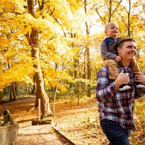Bright fall colors surround a young father and his toddler son as they walk through a forest
