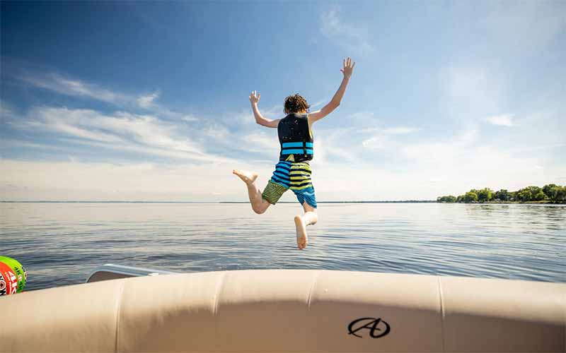 A boy wearing a life jacket jumps from an inflatable raft into a calm lake on a summer day