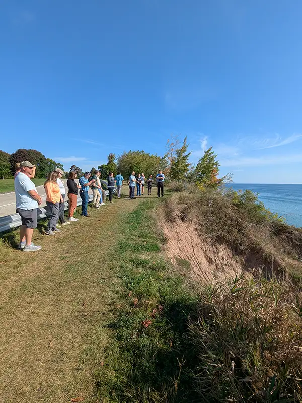 A group of people standing at the top of an eroding coastal bluff.